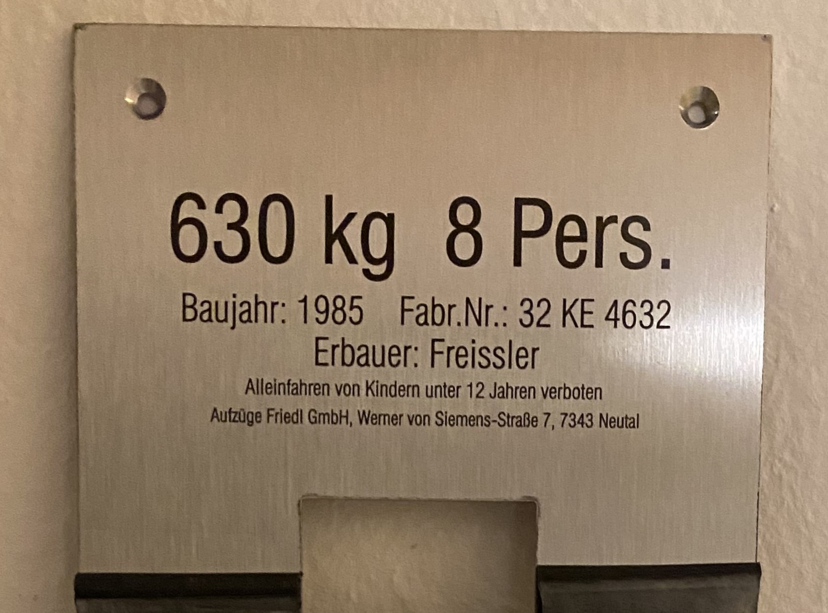 Schild mit Aufzugdetails: Kapazität 630 kg, Baujahr 1985, Hersteller Freissler, max. 8 Personen, Kinder unter 12 nicht allein.