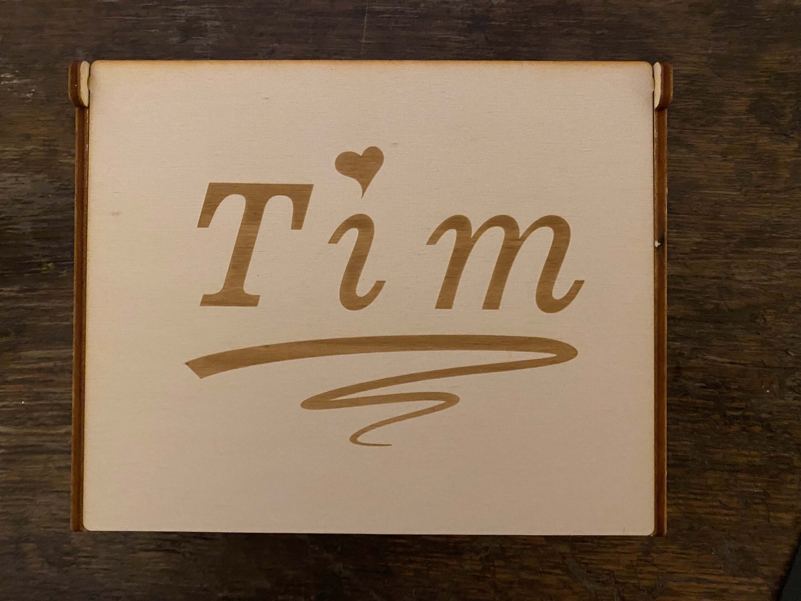 Personalisierte Holzkiste mit der Aufschrift Tim und Herzmotiv auf dunklem Holztisch.