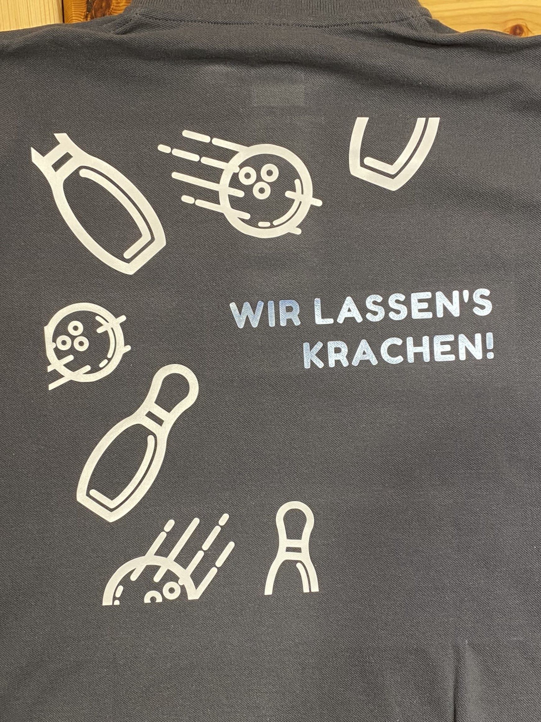 Schwarzes T-Shirt mit Bowling-Design und dem Text Wir lassen's krachen! in weißen Buchstaben.