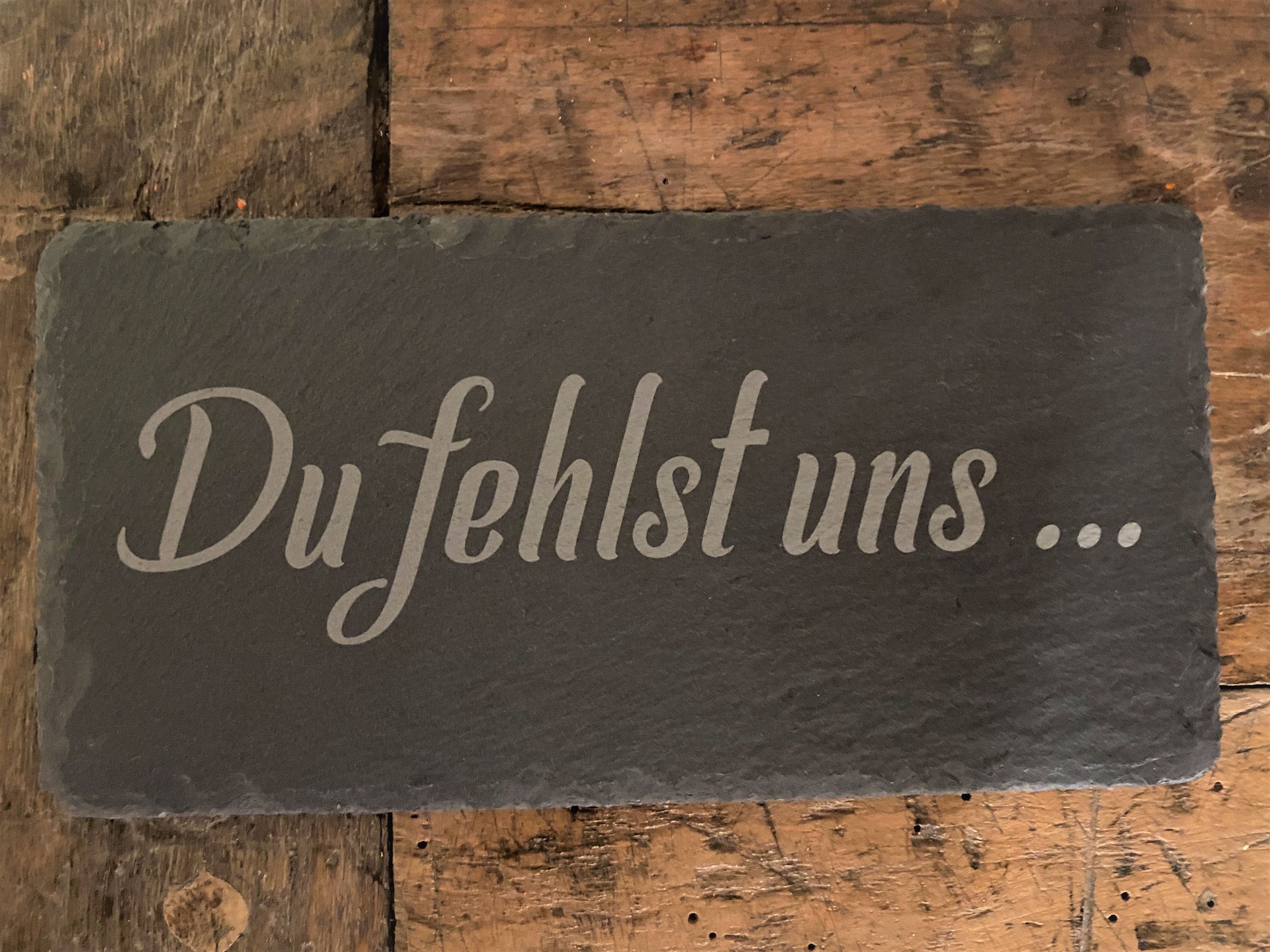 Tafel auf Holzuntergrund mit Schriftzug Du fehlst uns... - Erinnerung und Sehnsucht ausdrückend.