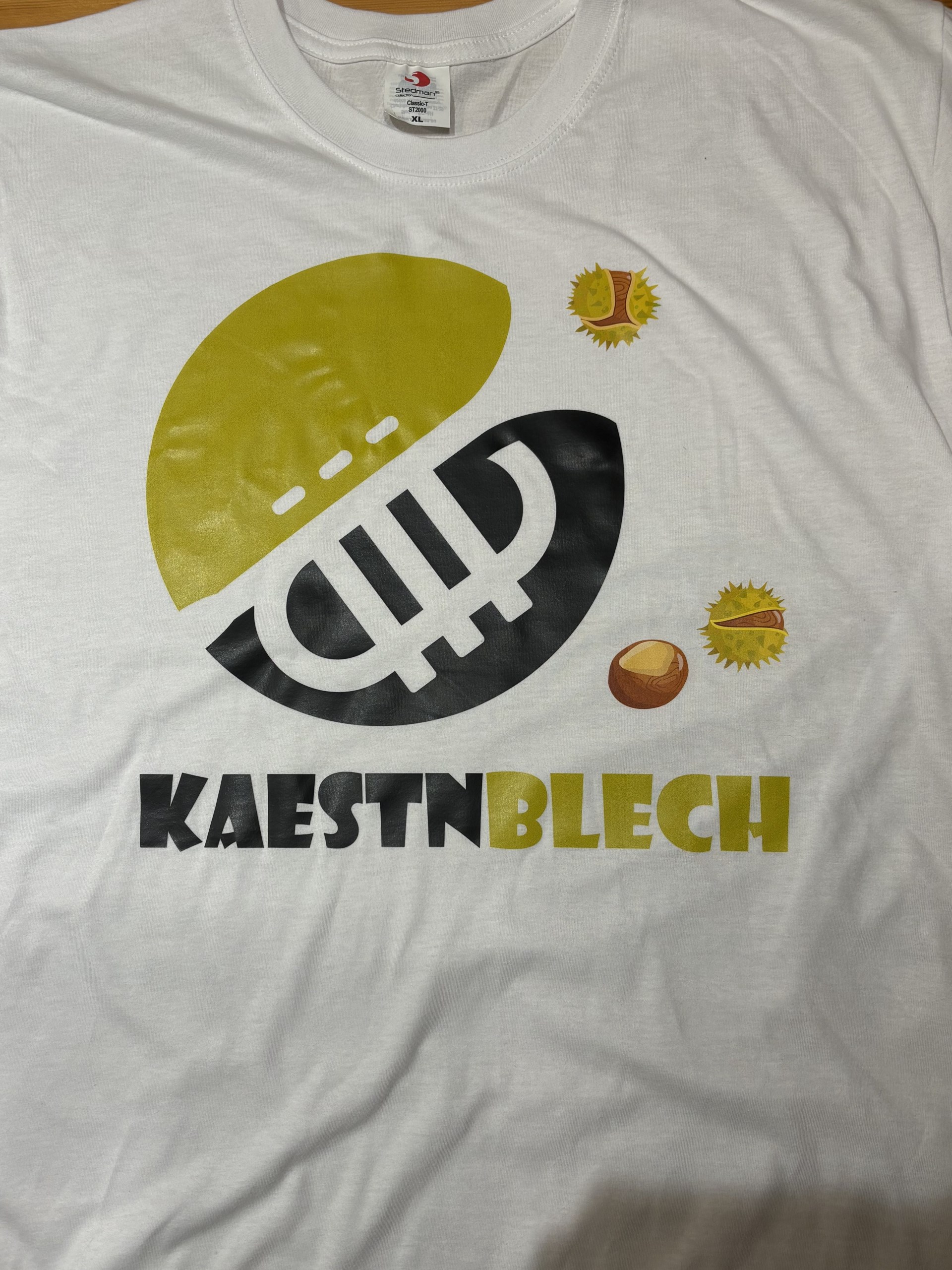 Weißes T-Shirt mit Kaestnblech-Design in Gelb und Schwarz, illustrierten Kastanien und Logo.